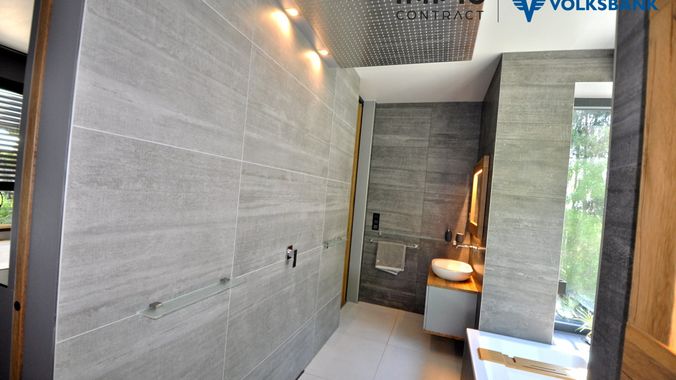 Badezimmer 2 OG mit Dusche vor der Wanne und großer Glasfront mit Blick in den Wald während dem Duschen